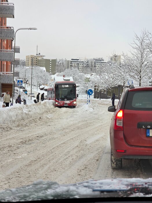 Snöig gata blockerad av trafikerad buss och bil, gångtrafikanter i snön.
