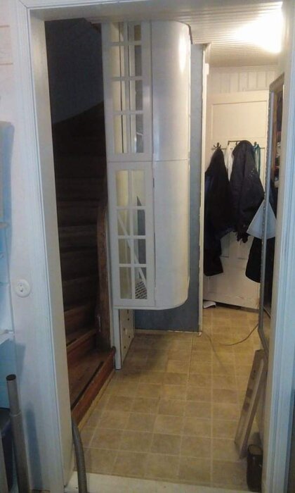 Hemgjord hiss installerad inomhus bredvid en trappa, med glasade dörrar och vit finish.