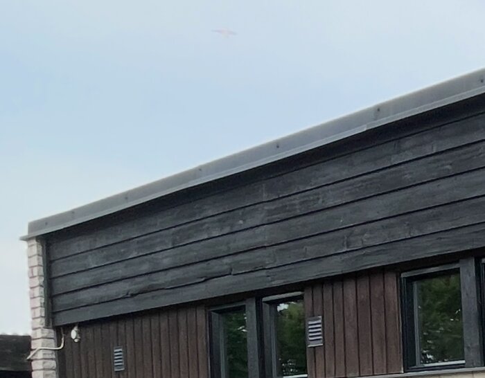 Fasaden på ett hus med ett platt papptak och mörkt träpanel, där plåten längs kanten är nyrenoverad.