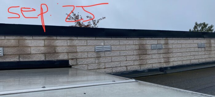 Fasad med fuktfläckar under takkant och ovanför plåt, markerat med röd text "sep: 25". Dagbild med molnig himmel i bakgrunden.