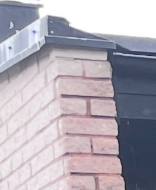 Tegelfasad med ny plåtinstallation som visar kantskarv och hörnavslutning. Problem med fukt och exponerade delar av fasaden efter renovering.