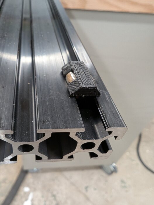 Svart aluminiumprofil med monterad T-mutter på ett fräsbord, del av ett gör-det-själv-projekt med inslag av anpassningar och förbättringar.