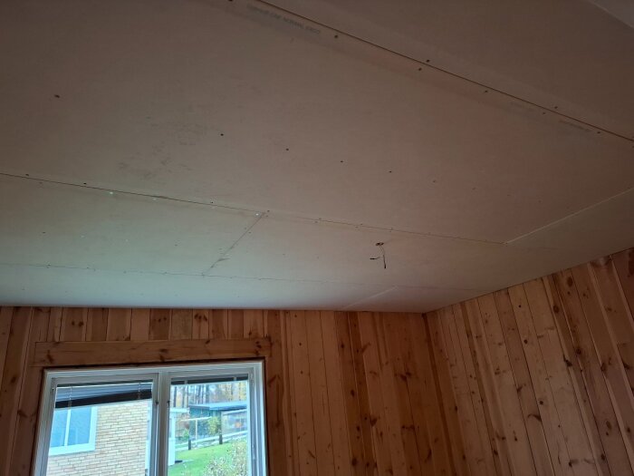 Gipsskivor monterade i taket över ett rum med träpanel, renovering av dotters rum.