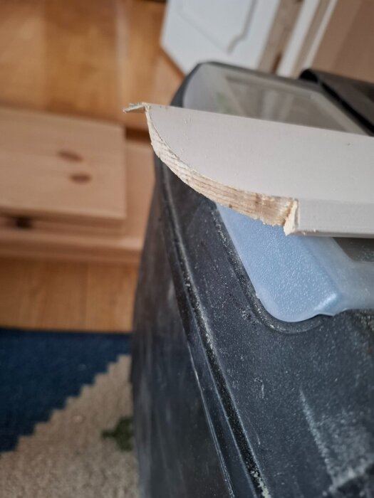 Närbild av en snedskuren listbit på en svart yta, med golvplankor i bakgrunden.