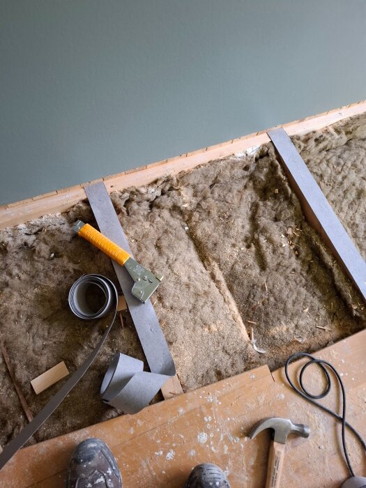 Verktyg och material för golvinstallation, inklusive en hammare, såg och skärverktyg, samt borttaget golv och synligt isoleringsmaterial.