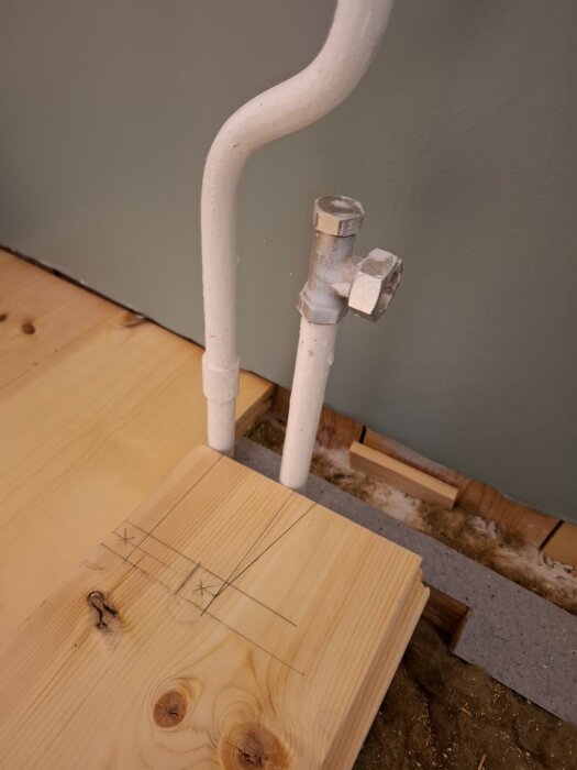 Massivt furugolv med markerade linjer för röruttag, bredvid ett målat rör i ett rum under renovering.