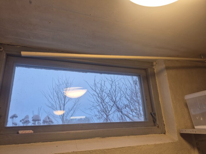 Vattenrör går längs väggen under ett fönster i en källare, synligt på vänster sida.