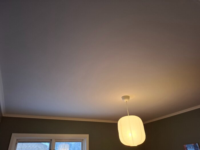 Taket i rum med hängande lampa, ljus färg, fönsterdel synlig.
