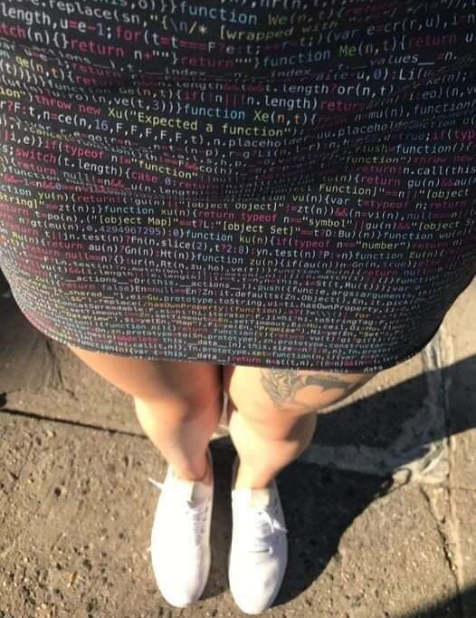 En kvinna som bär en klänning med kodmönster och vita sneakers.