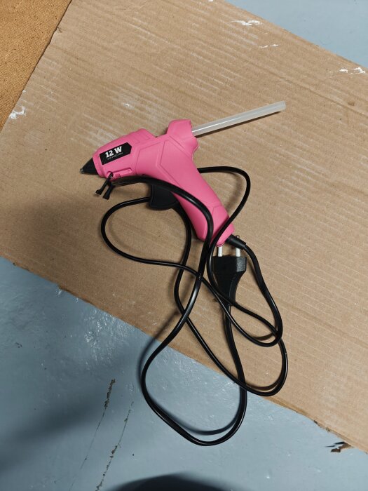 Rosa limpistol med kabel ligger på en kartongbit på ett grått golv.