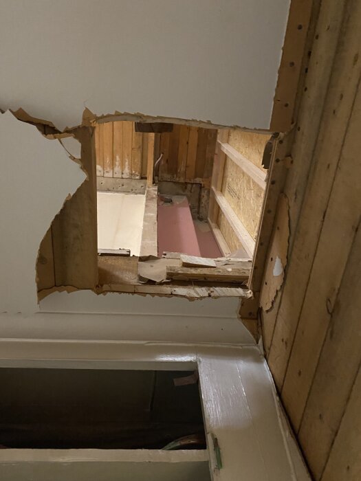 Utskjuret hål i ett innertak för planerat installationsschakt och tvättnedkast, omgiven av träpanel och vägg.