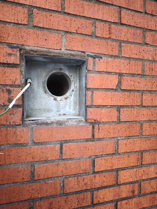 Öppning i tegelvägg för ytterväggsfläkt, med kanalrör som inte ansluter i fas, vilket skapar ett större glapp bakom fläkten.
