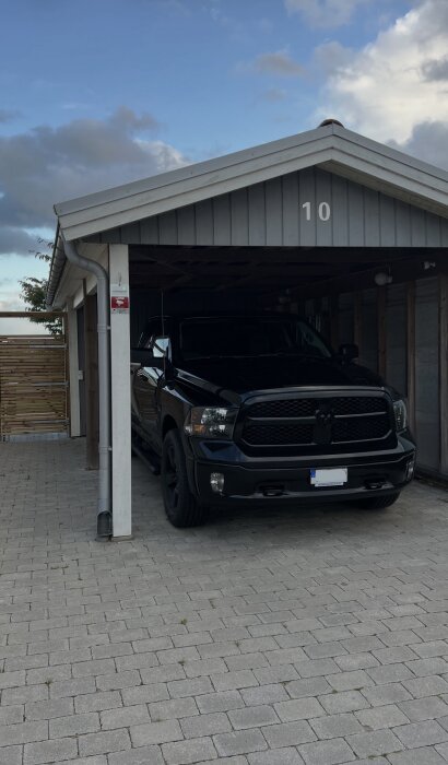 Carport med bil under, tak med stupränna till vänster, nummer 10 på gaveln.
