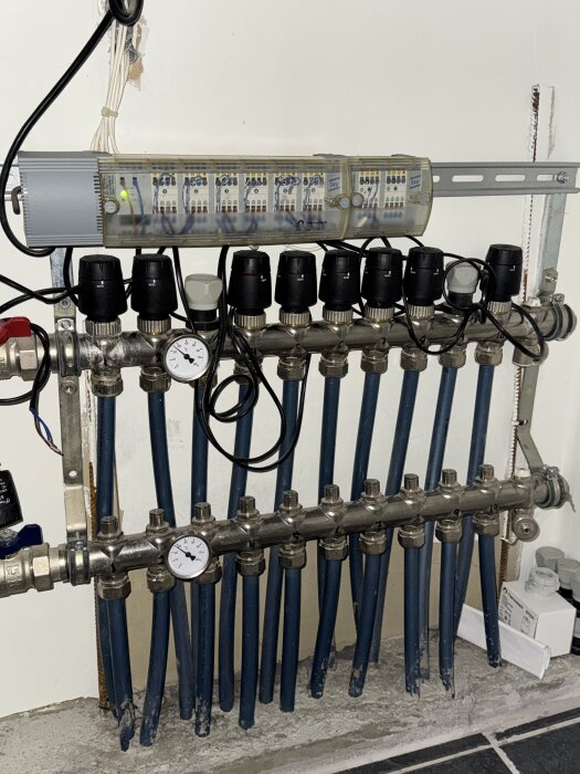 Värmesystem med avstängningsventiler, tryckmätare och slangar installerat på en vägg, del av ett äldre pumphus.