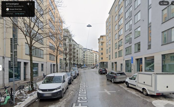 Gata med moderna flerfamiljshus i Stockholm, omgiven av parkerade bilar; vintertid med snöfläckar.