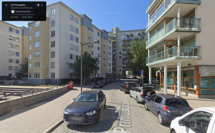 Gata i Stockholm kantad av moderna flerbostadshus, bilar parkerade längs trottoaren, solbelyst miljö.
