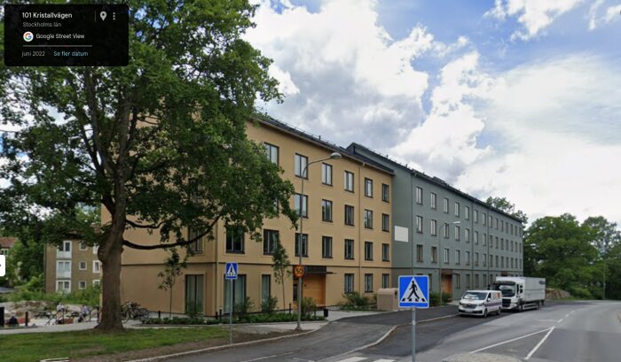 Gatubild av moderna bostadshus längs Kristallvägen i Stockholm, juni 2022, med närliggande grönska och fordon på vägen.