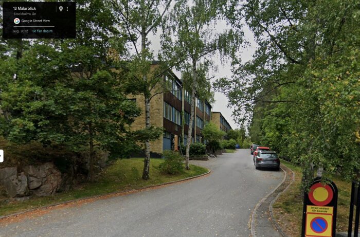 Gatulandskap i Stockholmförort med modernistiska flerbostadshus, träd längs vägen och parkerade bilar.