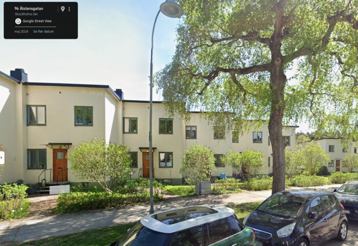 Rad av flerbostadshus i modernistisk stil med vita fasader, omgärdade av träd och parkering, i en Stockholmsförort.