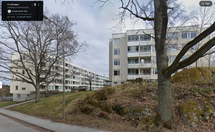 Vita flerfamiljshus i modernistisk stil i en Stockholmsförort, med träd och trottoar i förgrunden.
