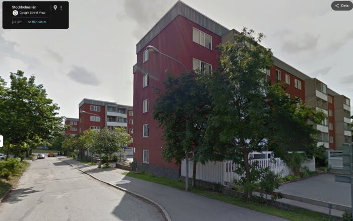 Modern flerfamiljshus i förort, Stockholm. Rött tegel, fönster och träd längs gatan.