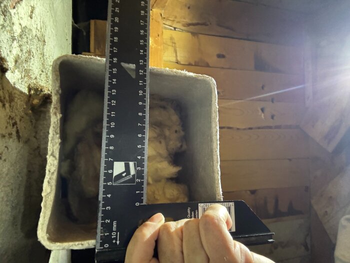 Gammal ventilationskanal mäts med linjal, omgiven av träpanel och murstock.