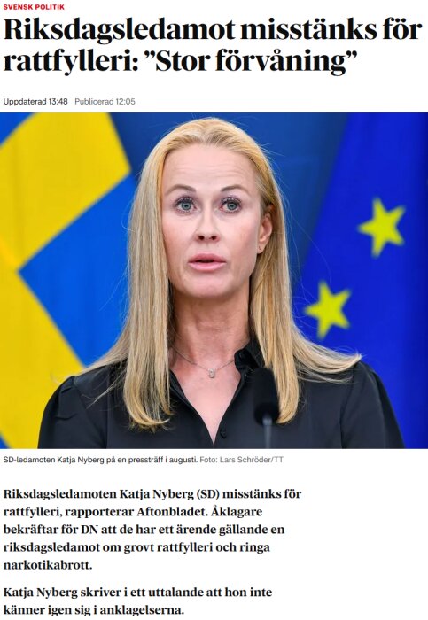 Kvinna talar på en presskonferens med en svensk flagga i bakgrunden. Hon ser förvånad ut.