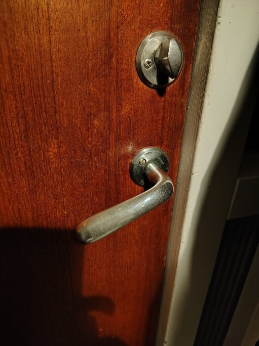 Trädörr med metallhandtag och vred, visar ett nedhängande dörrtrycke från 1970-talet.
