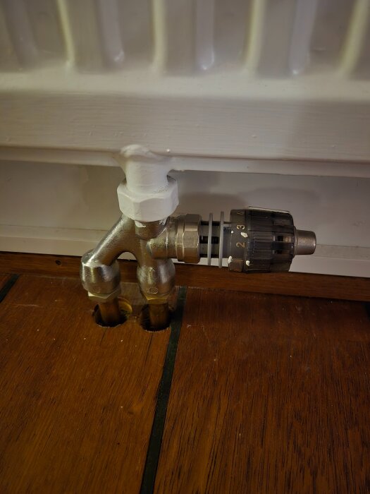 Ventil och röranslutning vid golvet under en radiator, med en synlig termostatinställning på 2.