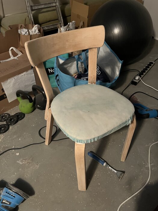 Trästol under renovering, med avskrapad färg och verktyg runt omkring. Stolsits klädd i ljusblått tyg.