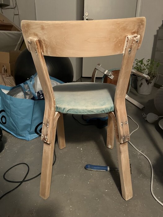 Trästol under renovering med borttagen färg, omgiven av verktyg på ett betonggolv.