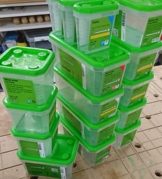 Plastburkar med gröna lock staplade på ett bord i ett garage eller verkstad.