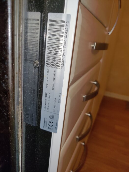 Serienummer och streckkod på sidan av en vit hushållsmaskin i kök.