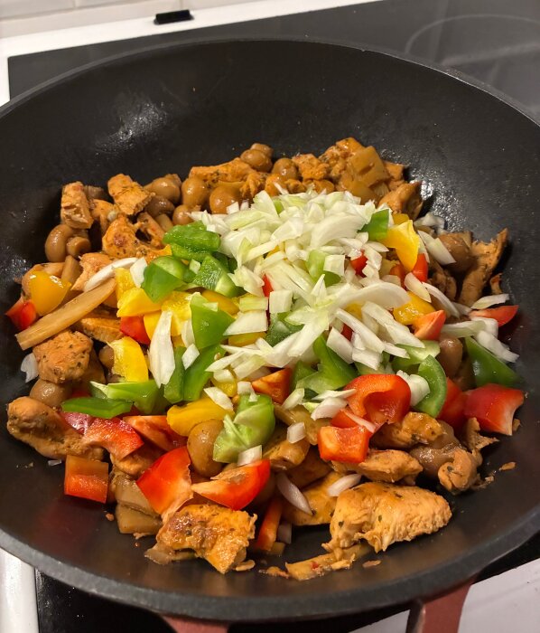 Gryta med Chicken Korma, innehållande kycklingbitar, röd, grön och gul paprika, lök och svamp i en stekpanna.