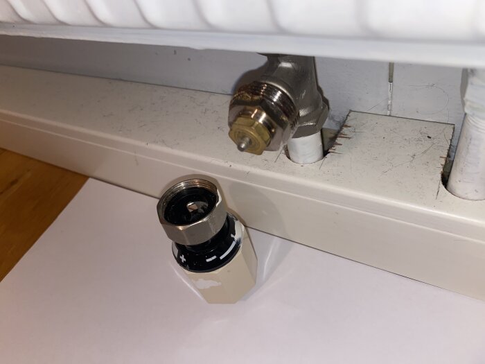 Närbild av en avmonterad termostatventil framför en radiatoranslutning.