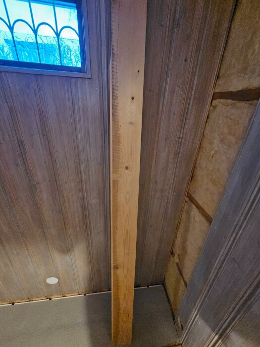 Träpanel med missfärgning i ett hörn bredvid isolering och fönster, del av renoveringsprojekt där innervägg ska rivas och isoleras på nytt.