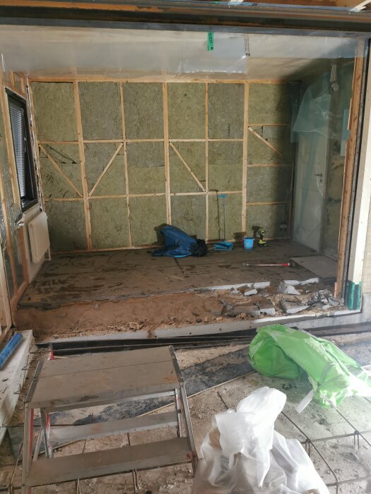 Insidan av en innervägg från ett hus byggt 1964 med synlig isolering och träreglar under renovering.