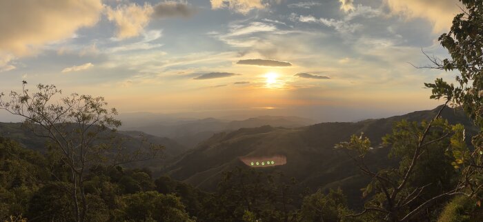 Solnedgång över berg och skog i Monteverde, Costa Rica, med moln och solstrålar i bakgrunden.