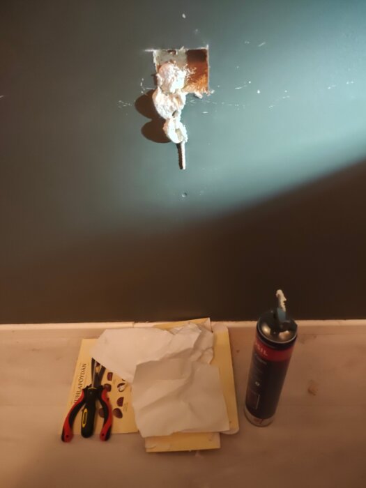 Vägg med hål fyllt med PU-skum. Verktyg och papper syns på golvet.