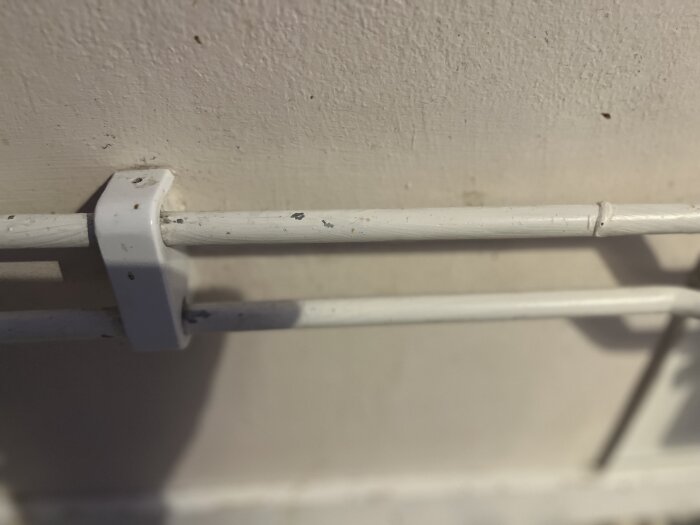 Vita rör monterade på en vägg med avskavd färg; fokus på skavmärken och fästklammer.
