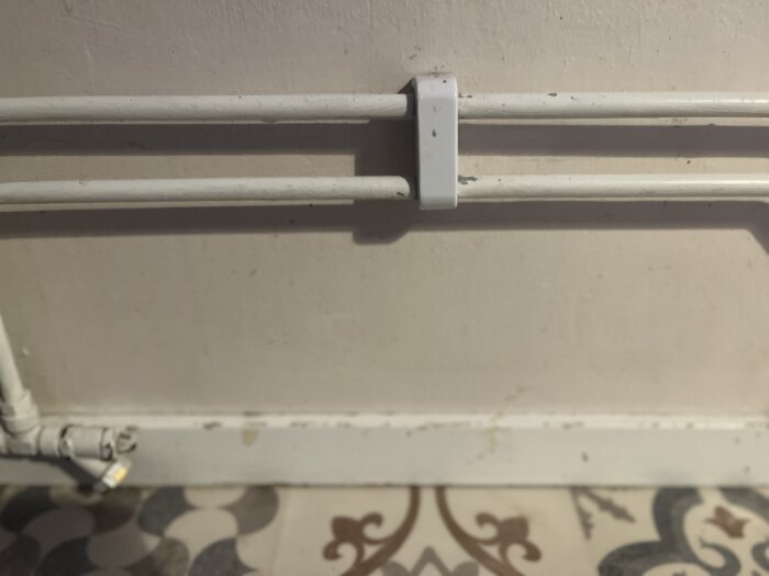 Avskavd vit färg på målade rör och golvlist i en bostad. Detalj av mönstrat golv under rören.