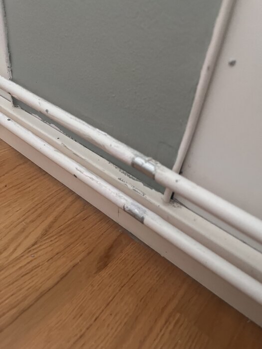 Vita målade rör med avskavd färg intill en vägg och golv av träparkett.