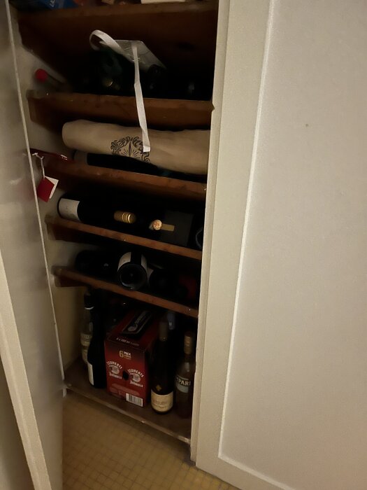 Litet äldre skafferi med trähyllor innehållandes vinflaskor och andra drycker, del av renoveringsprojekt för att förvara torrvaror.
