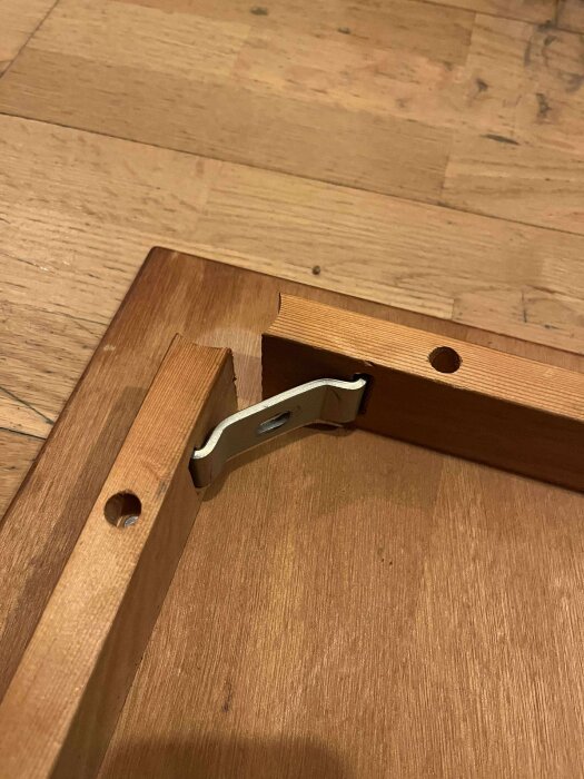 Hörnet av ett soffbord med ett beslag monterat men inget ben fäst, träytor och hål synliga.