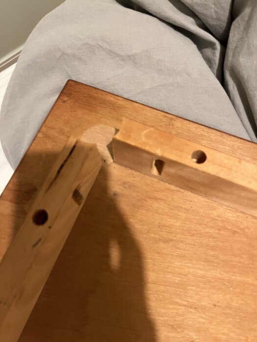 Trädelar med borrade hål, troligen en del av en träkonstruktion eller möbelmontering, mot en grå bakgrund.