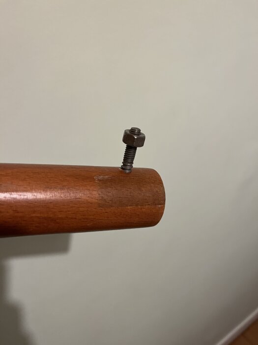 Träcylinder med genomgående skruv och mutter på dess ände, mot en beige bakgrund.