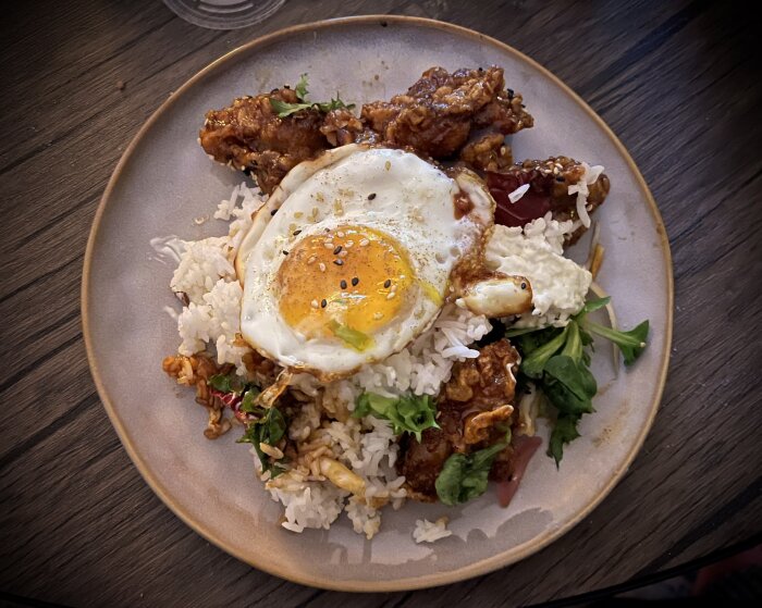 Koreansk mayo-kyckling med ris, stekt ägg, sallad och teriyakisås på en tallrik, toppad med sesamfrön.