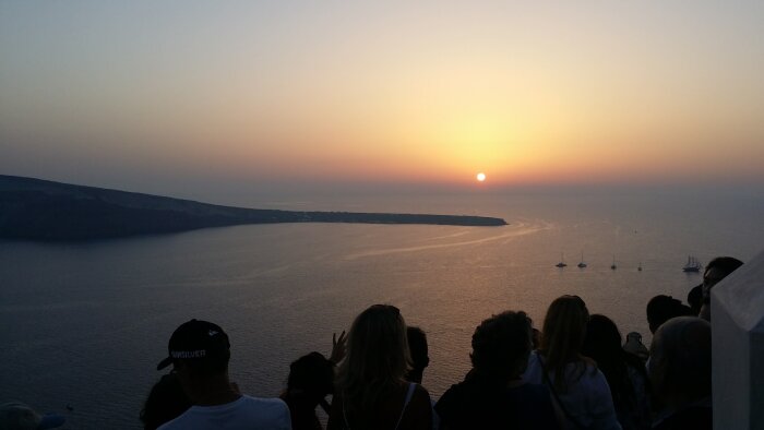 Solnedgång över havet på Santorini, Grekland, med en folksamling som tittar.
