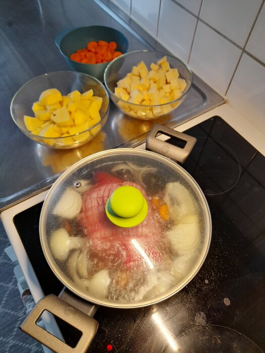 Kastrull med fläsklägg och grönsaker på spisen, samt skålar med tärnad potatis, kålrot och morötter på köksbänken.
