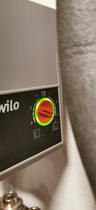 En vattenpump med ett rött reglage inställt på 3, omgiven av en grön lysning och symboler tryckta på panelen.